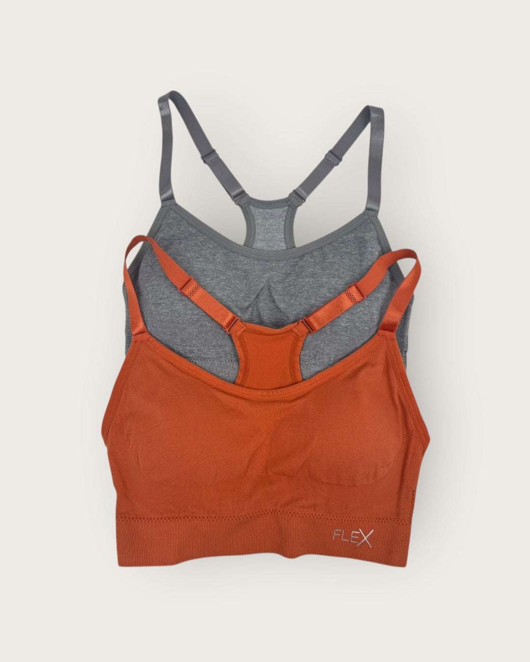 Two sports bras, one orange and one gray, on a light beige background.