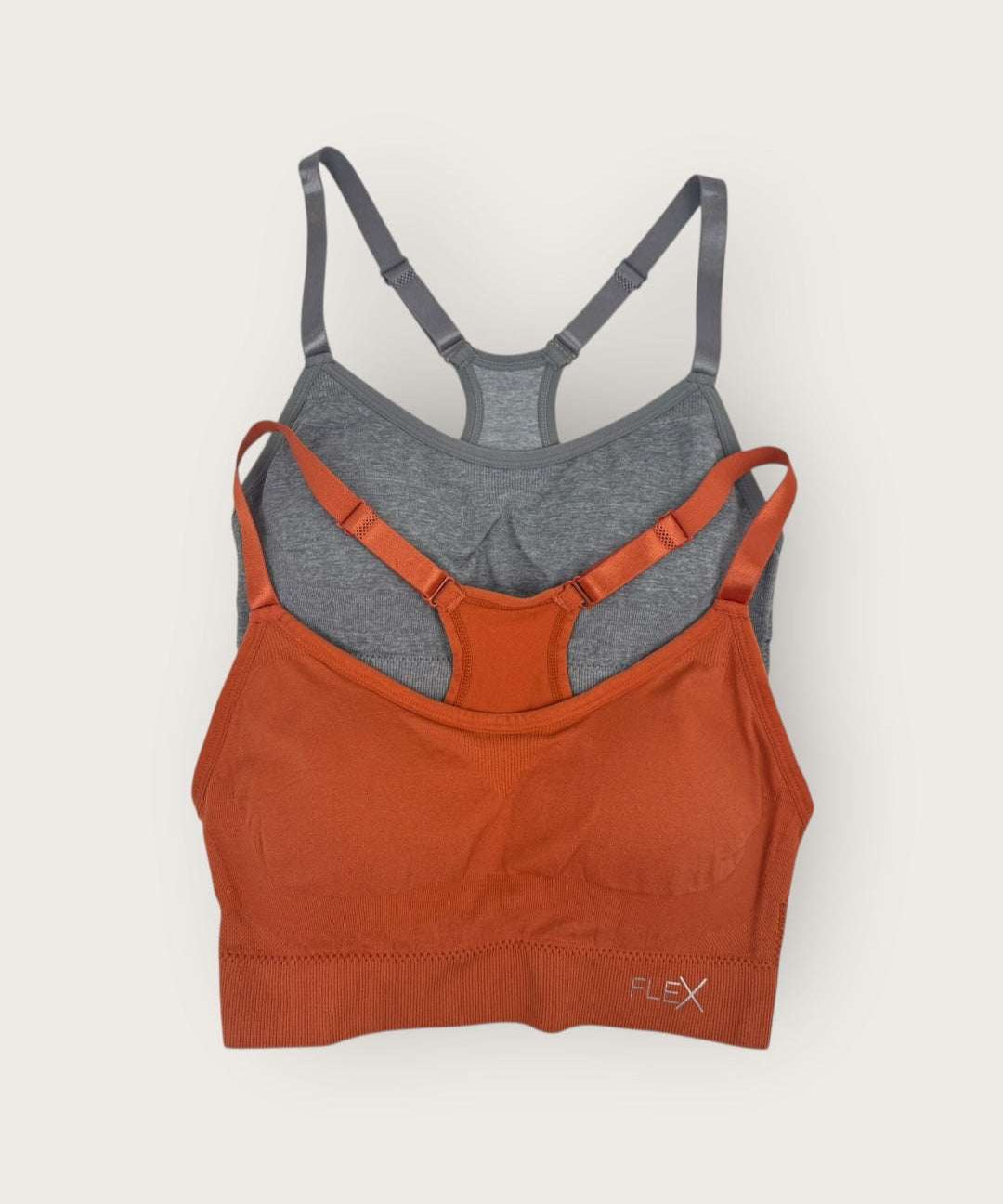Two sports bras, one orange and one gray, on a light beige background.
