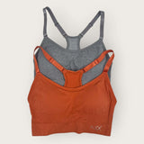 Two sports bras, one orange and one gray, on a light beige background.