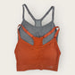 Two sports bras, one orange and one gray, on a light beige background.