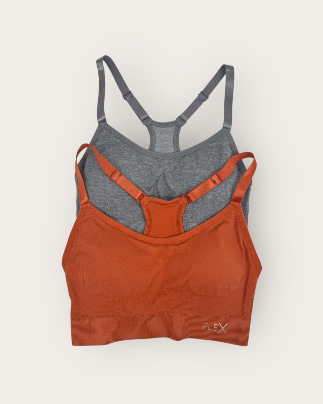 Two sports bras, one orange and one gray, on a light beige background.