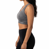 Woman wearing a gray sports bra and black leggings on a white background