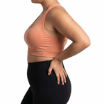 Woman wearing a peach sports bra and black leggings on a white background