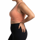 Woman wearing a peach sports bra and black leggings on a white background