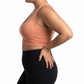 Woman wearing a peach sports bra and black leggings on a white background