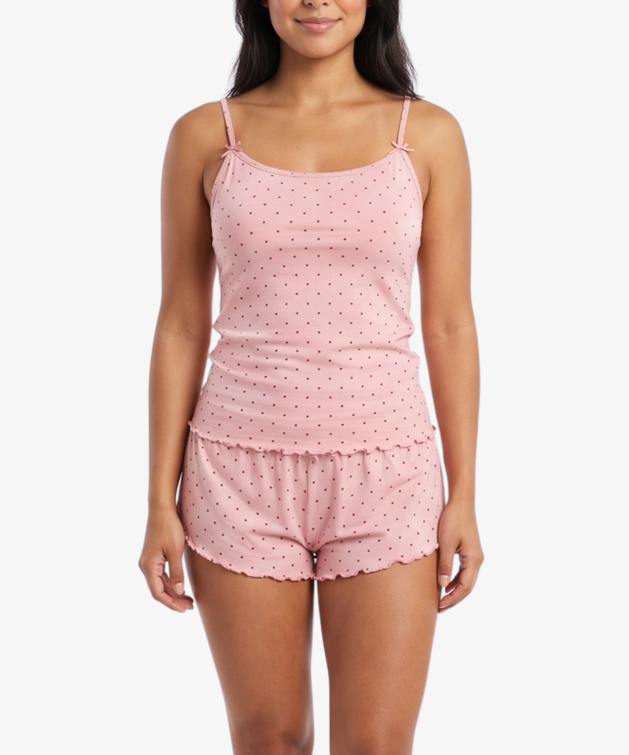 A woman modeling a light pink two-piece pajama set with a small white floral pattern, consisting of a spaghetti-strap camisole top and matching ruffled shorts, against a plain white background.