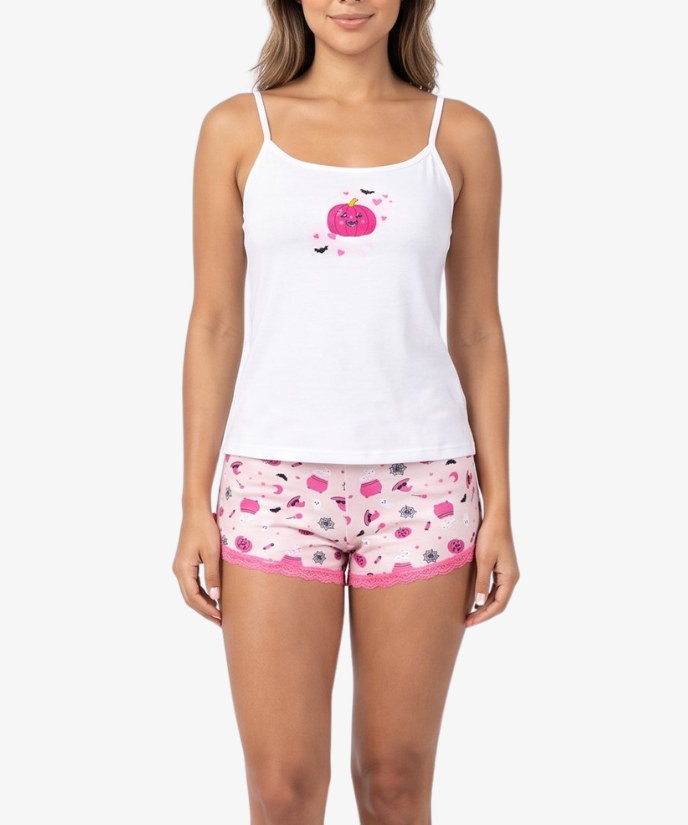 A woman modeling a two-piece pajama set consisting of a white tank top with a pink cherry graphic and matching pink patterned shorts, shot against a solid light gray background.