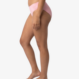 A woman modeling a light pink bikinis panty set against a plain light gray background.