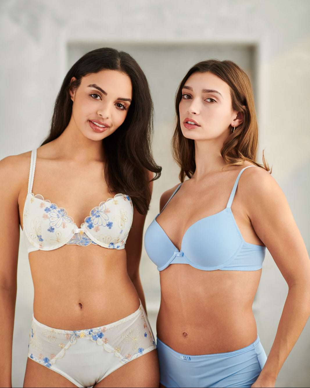Two women wearing floral and blue bras with matching panties against a plain background