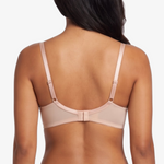 A woman shown from the back wearing a matching nude-beige bra and panty set with lace trim, against a plain light gray studio background.