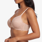 A woman modeling a light beige/nude lace bra and matching lace underwear against a plain light gray studio background.
