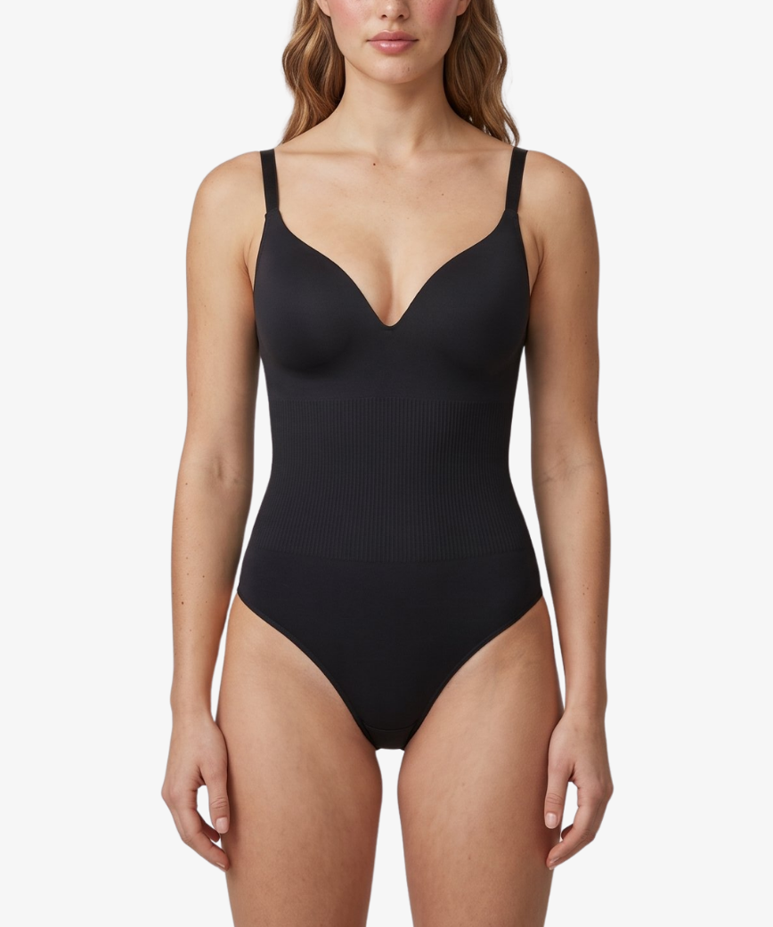 A woman modeling a black one-piece shapewear with thin shoulder straps and a deep V-neckline, photographed against a clean light gray studio background.