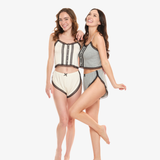 Two women in matching pajama sets behind a white background. One woman is wearing a cream pajama set and the other woman is wearing a gray pajama set.